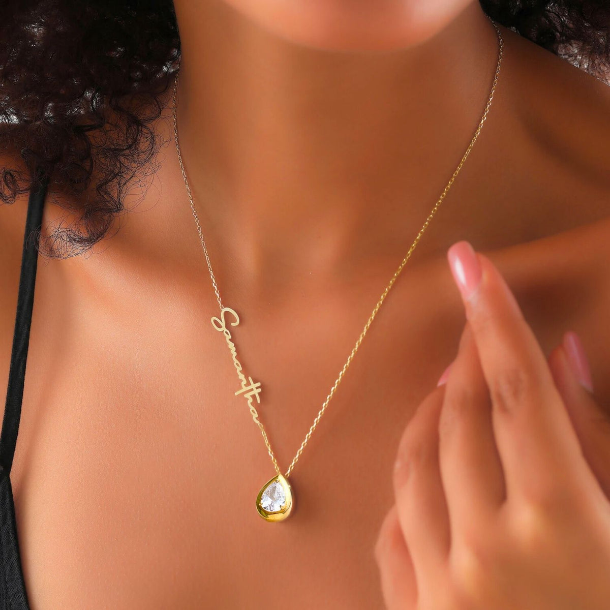 Gold necklace with a diamond pendant on a woman wearing a black top.