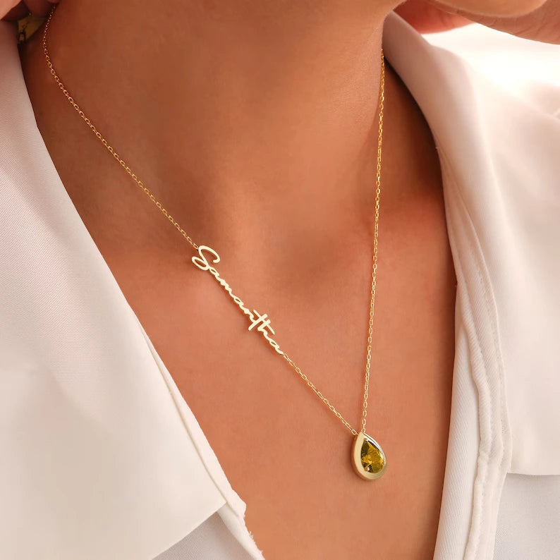 A woman showcasing a custom name necklace with a teardrop-shaped peridot gemstone and personalized engraving on the chain.