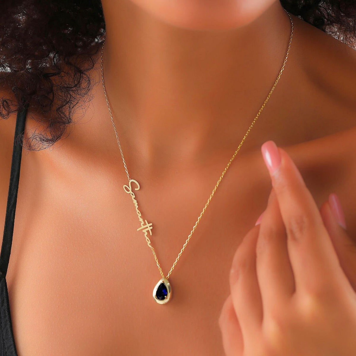 Gold necklace with a sapphire gemstone pendant on a woman wearing a black top.
