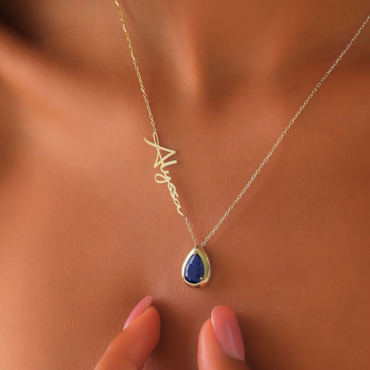 Gold necklace with a sapphire teardrop pendant on a woman's neck
