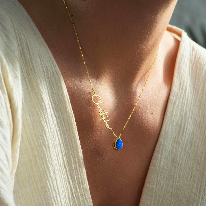 Gold necklace with a blue opal pendant on a woman wearing a white top.