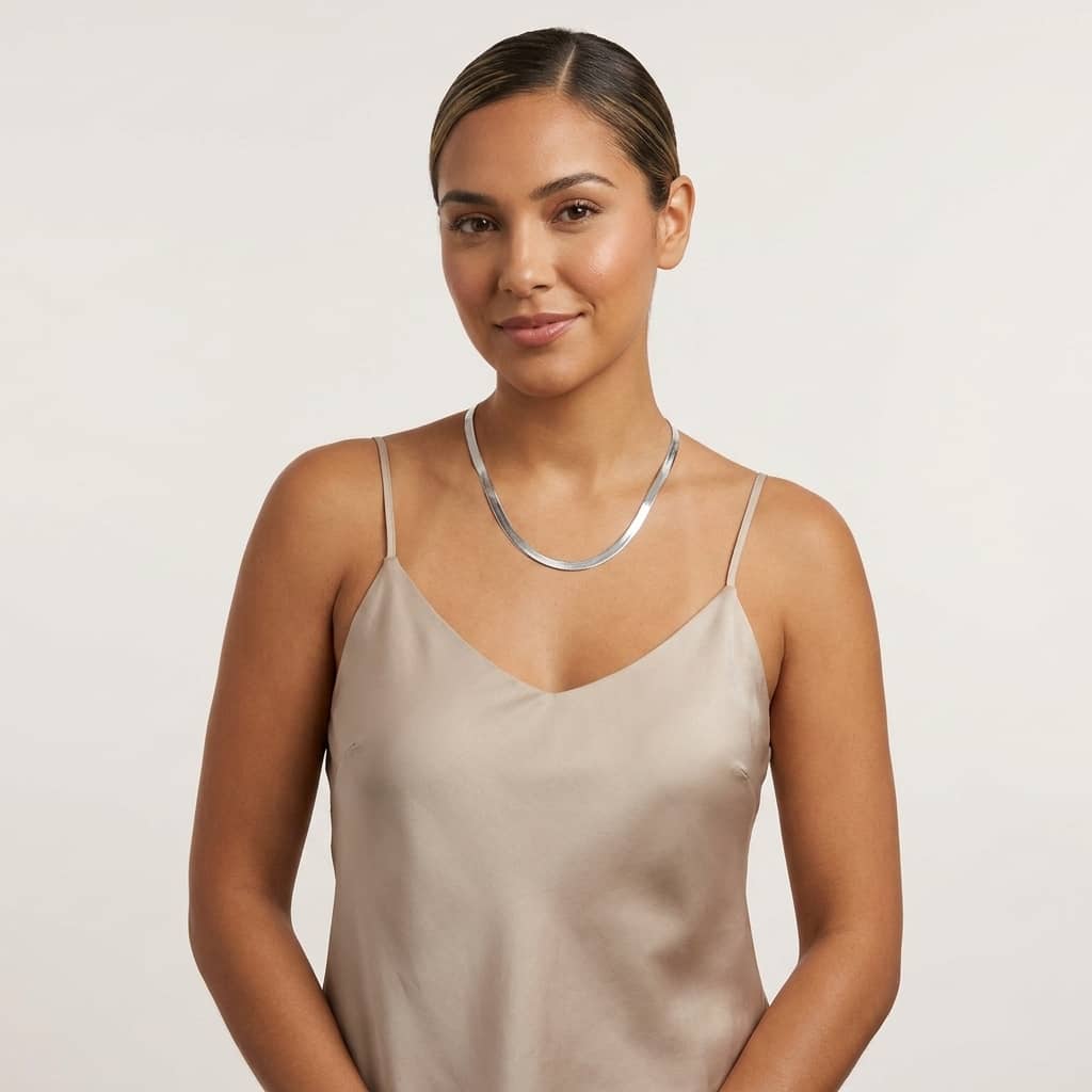 A woman modeling a classic silver-toned herringbone necklace against a plain light background.