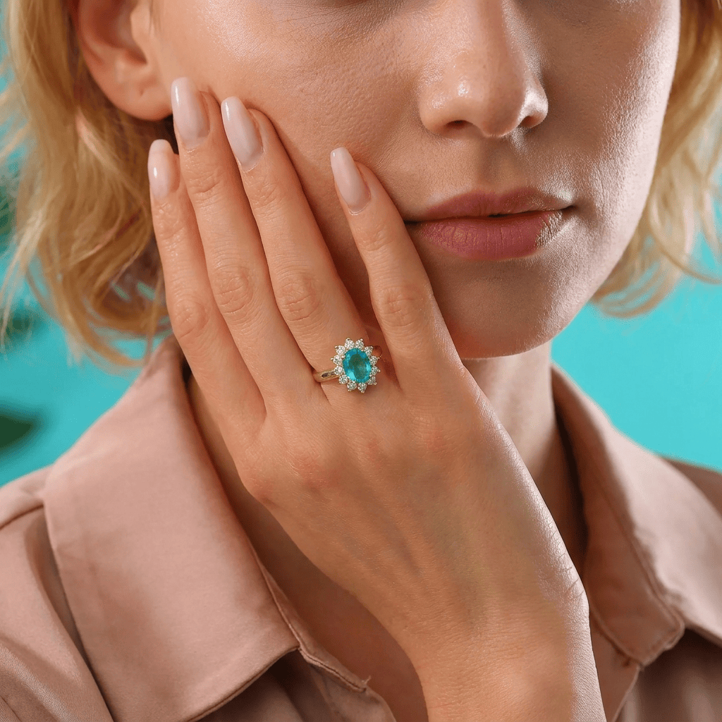 Close-up portrait of a blonde woman in a dusty rose blouse wearing the gold blue topaz halo December birthstone ring.