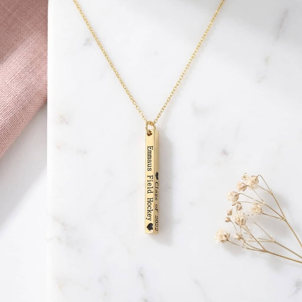 Gold necklace with a bar pendant on a marble surface with dried flowers.