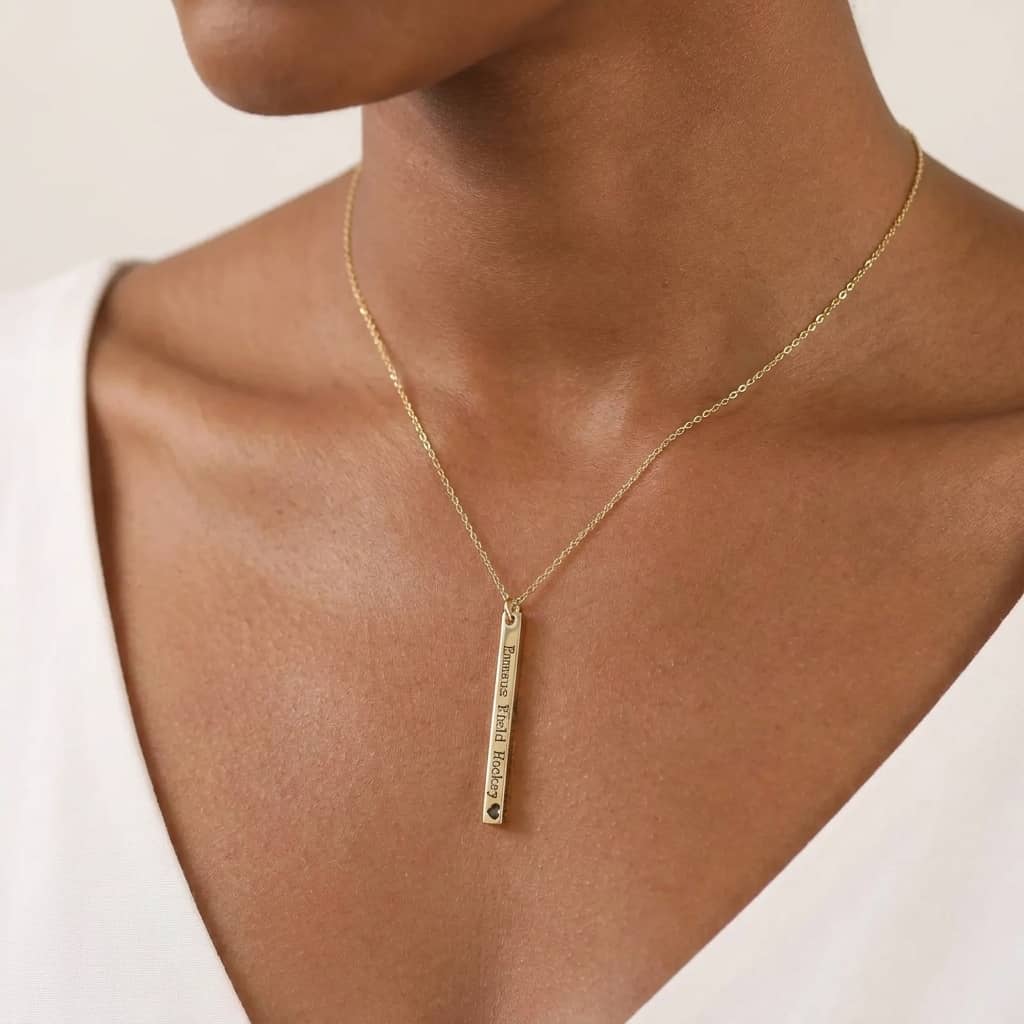 Gold necklace with a bar pendant on a woman wearing a white top.