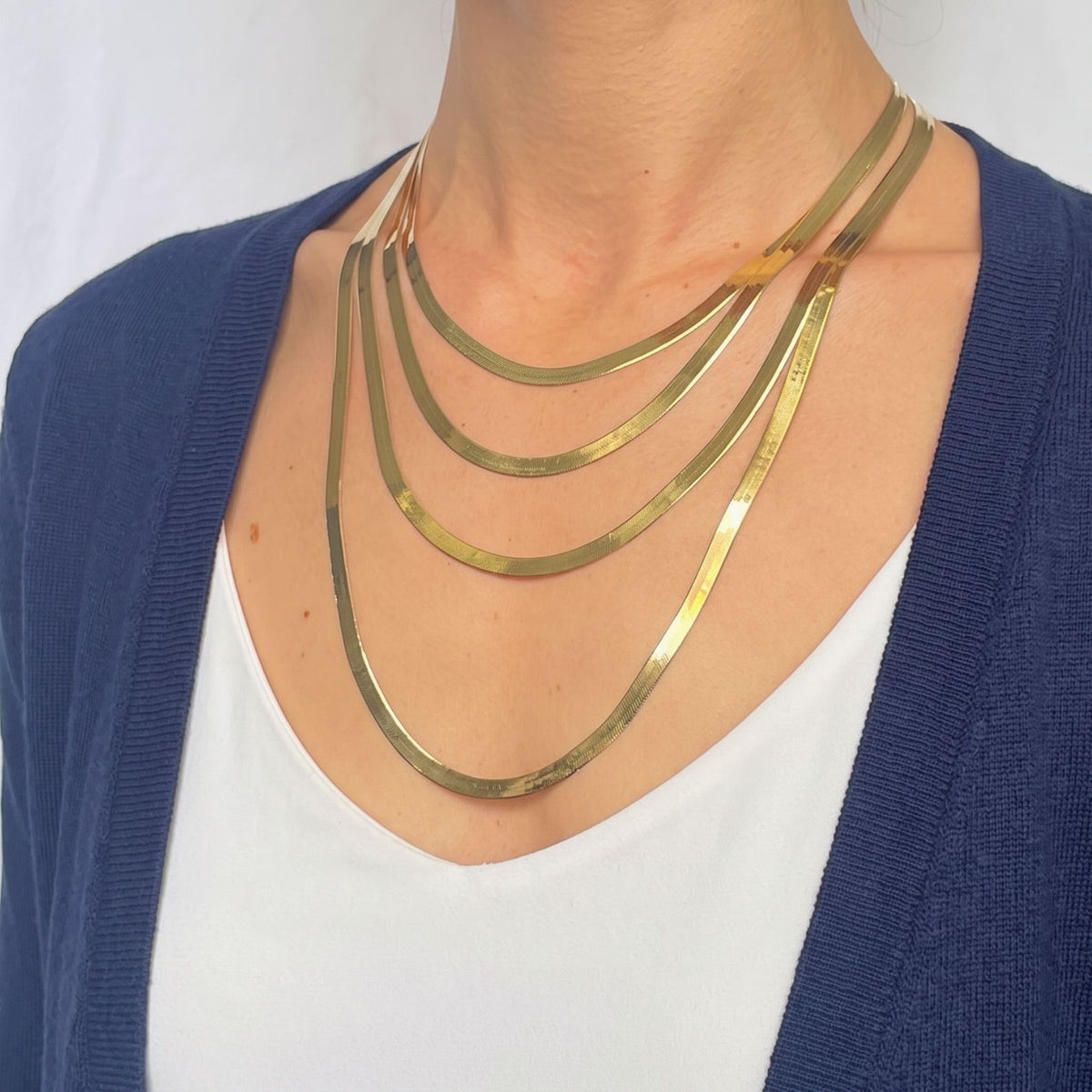 Model wearing four graduated layers of yellow gold herringbone necklaces against a navy cardigan