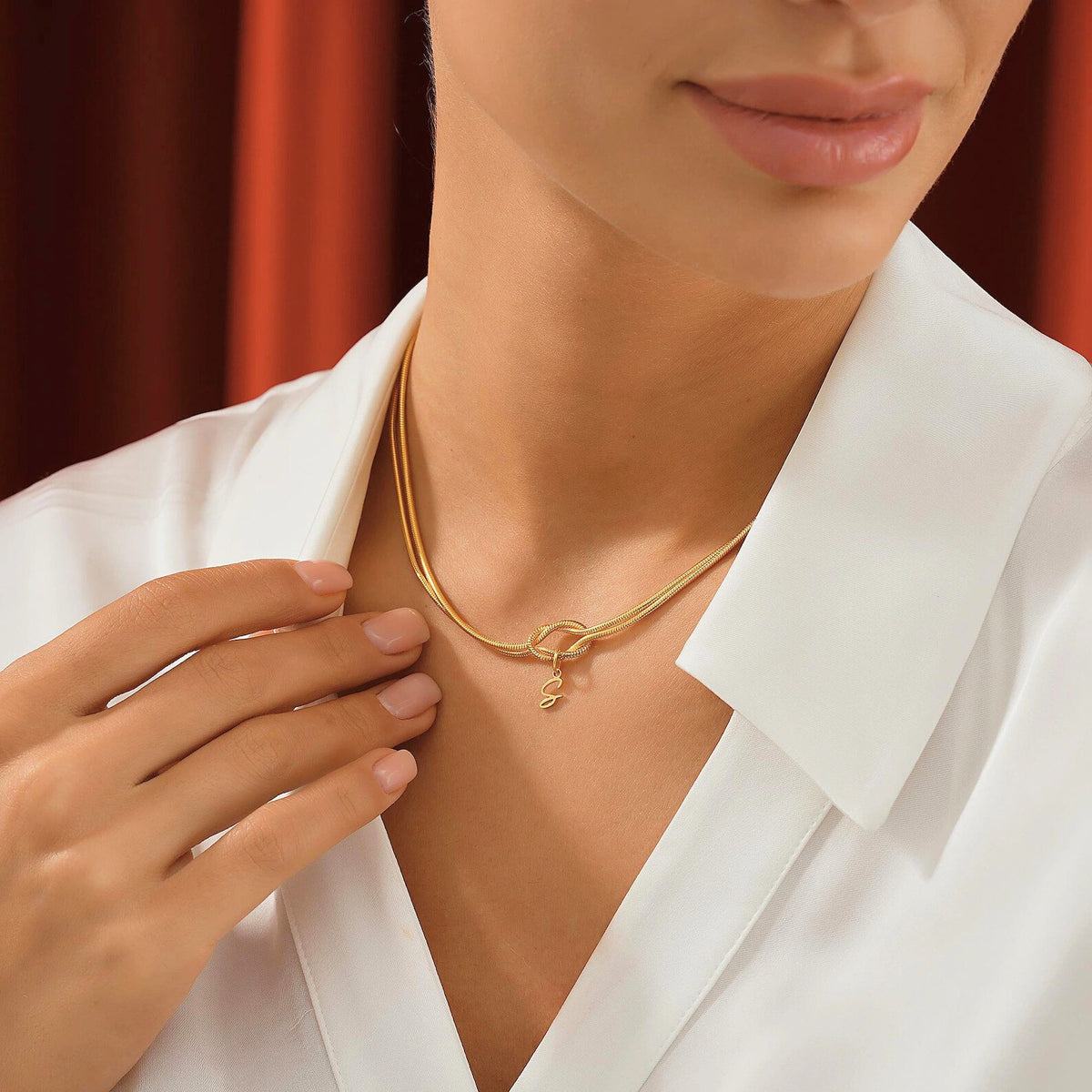 Gold love knot initial necklace on model’s neck with double snake chain choker style