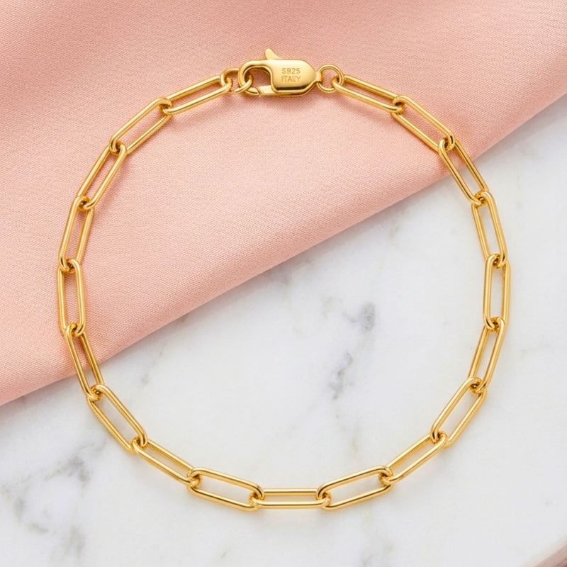 Detailed close-up of a high-shine gold paperclip chain bracelet lying on a rustic neutral linen surface