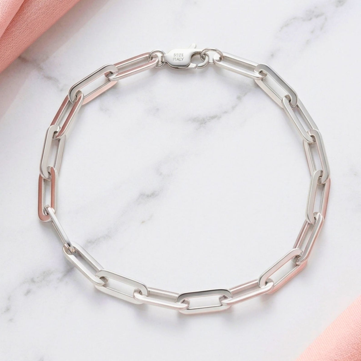 Elegant sleek polished silver paperclip bracelet on a minimal light grey backdrop, emphasizing minimalist luxury