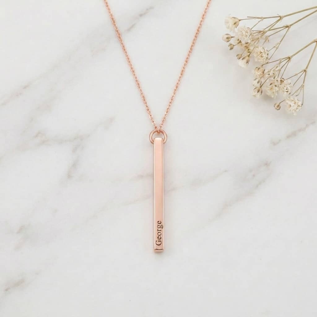Rose gold necklace with a vertical bar pendant on a marble surface with dried flowers.