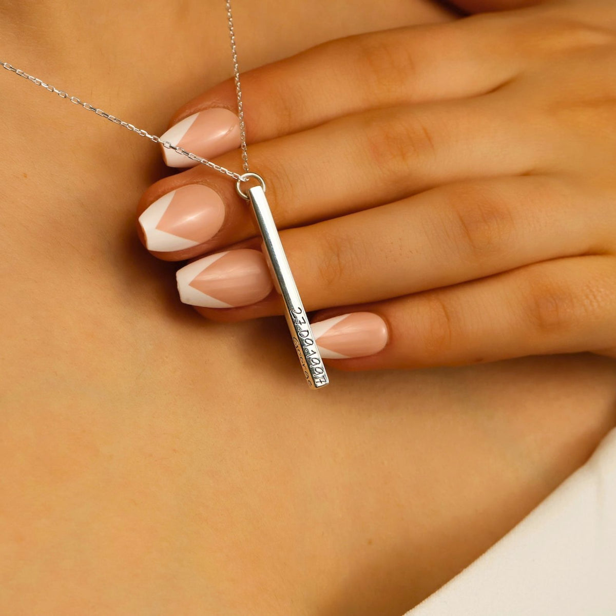 Silver necklace with a bar pendant held by a woman's hand.